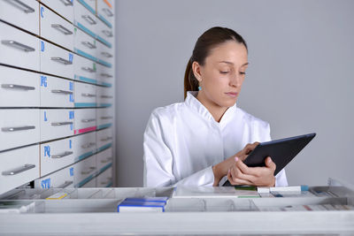 Young woman wearing lab coat while using digital tablet