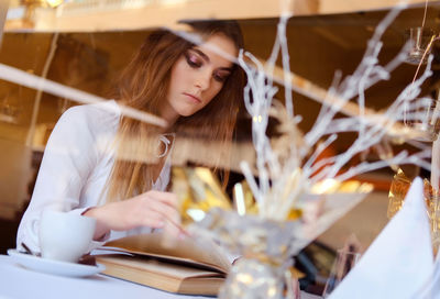 Teenage girl reading book seen through window