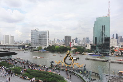 People on river by buildings in city against sky