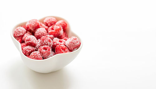Close-up of frozen raspberries in bowl against white background.