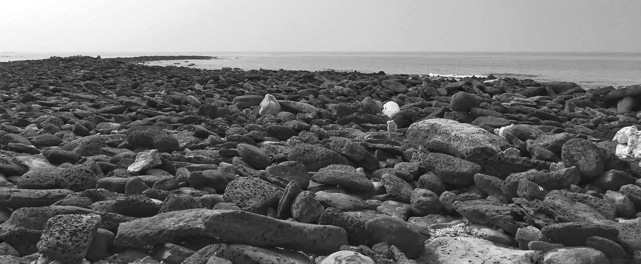sea, horizon over water, beach, water, shore, pebble, tranquility, tranquil scene, nature, rock - object, clear sky, stone - object, beauty in nature, scenics, abundance, sky, copy space, day, outdoors, idyllic