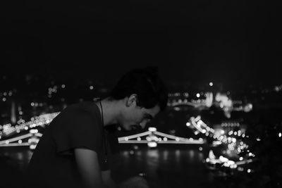 Side view portrait of young man playing in illuminated city at night