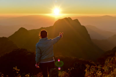 Rear view of woman pointing at mountains during sunset