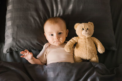 Baby boy is lying on a pillow with a soft teddy bear and covered with a blanket