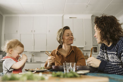 Smiling lesbian couple with daughter having lunch at home