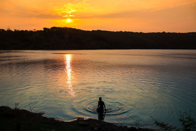 Silhouette man standing by lake against sky during sunset