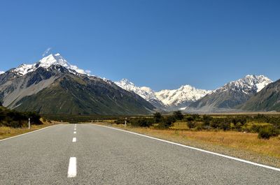 Road amidst snowcapped mountains against clear blue sky