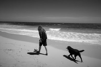 Full length of man with dog at beach against sky