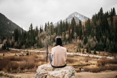 Rear view of woman sitting against trees