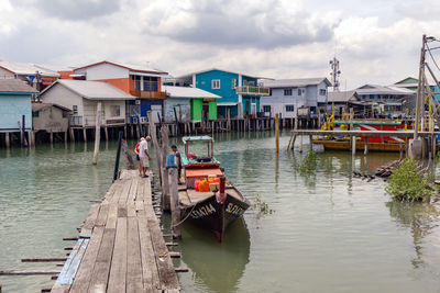 Boats moored in canal by houses against sky