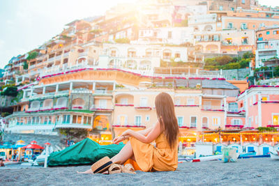 Side view of woman sitting against buildings in city