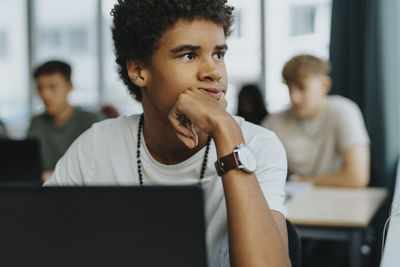 Thoughtful teenage boy with hand on chin in classroom