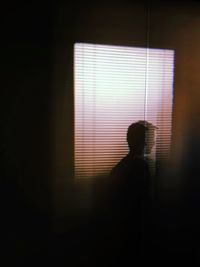 Silhouette man standing against window in dark room