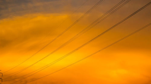 Low angle view of power lines against orange sky