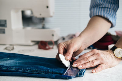 Cropped hands of tailor marking jeans with chalk on table in workshop