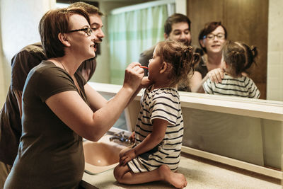 Father standing by mother brushing teeth of daughter in bathroom