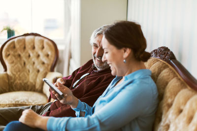 Happy senior man using smart phone with daughter in living room