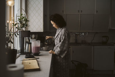 Mature woman pouring coffee in cup at kitchen counter