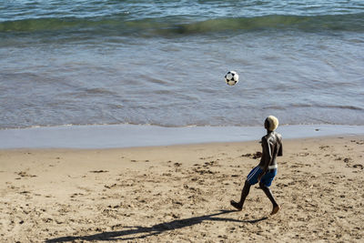 Full length of boy playing soccer at beach