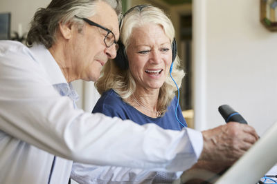 Smiling senior friends with microphone and headphones vlogging at home