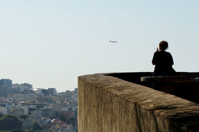 Rear view of woman smoking by retaining wall against sky