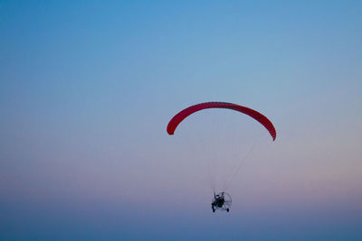 Low angle view of people paragliding against clear sky