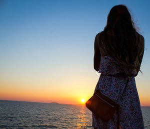 Rear view of woman standing by sea against sky during sunset