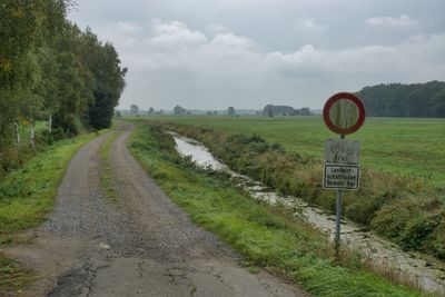 Road passing through field against sky