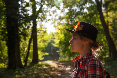 Side view of young woman standing against trees
