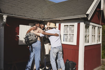 Smiling friends hugging in front of wooden house