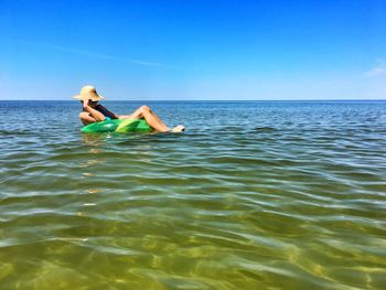 Woman relaxing in inflatable ring on sea against sky