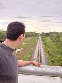 Side view of young man on railroad track against sky