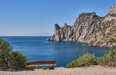 Seascape, crimean peninsula. a wooden bench stands on the shore of the blue bay.