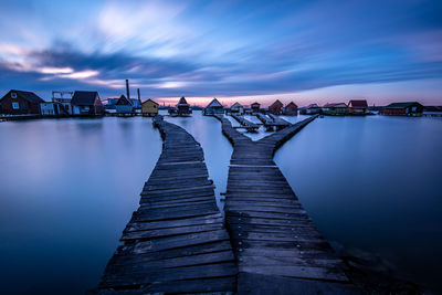 Pier over river against sky at dusk