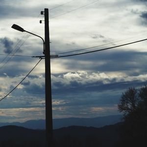 Low angle view of electricity pylon against cloudy sky