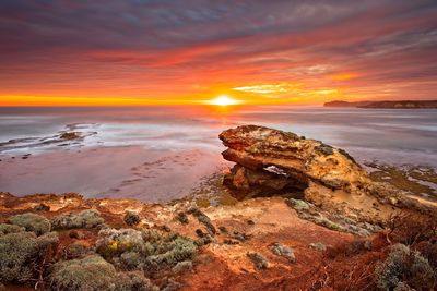 Rock formation on beach against sky during sunset