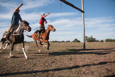 Men riding horses on field against sky