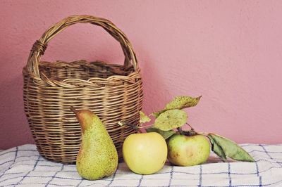Fruits by wicker basket against pink wall on table