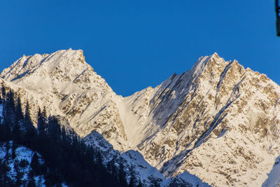 Low angle view of snowcapped mountains against clear blue sky