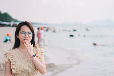 Portrait of beautiful woman wearing sunglasses gesturing while standing at beach