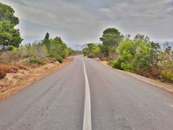 Empty road amidst trees against sky