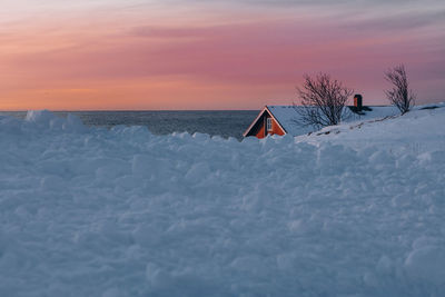 Snow covered land and sea against sky during sunset