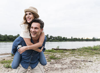 Happy man carrying girlfriend piggyback at the riverside