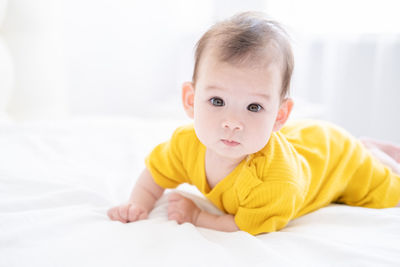 Healthy asian baby girl 5 months in yellow bodysuit on bed on white bedding