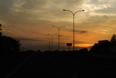 Road by silhouette trees against sky during sunset