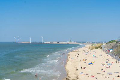 People at beach against clear blue sky