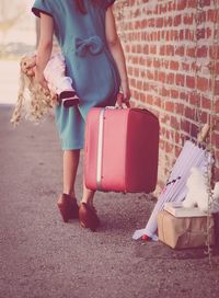 Low section of girl carrying doll and briefcase by brick wall