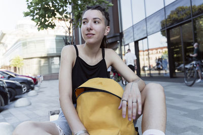 Contemplative non-binary person with backpack sitting on bench