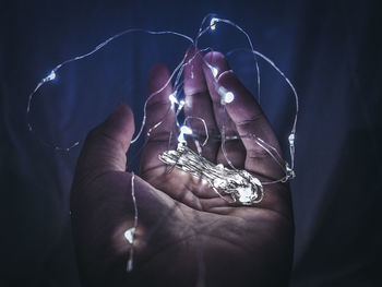 Cropped hand holding illuminated string lights in darkroom