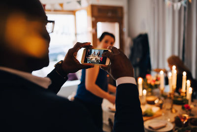 Man photographing friends through smart phone at dinner party